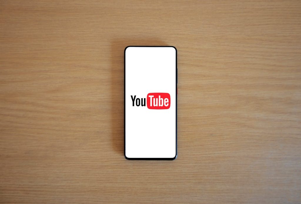 A phone on a wooden table with a Youtube logo displayed on screen. This is the fifth choice of the side hustle ideas on this list.