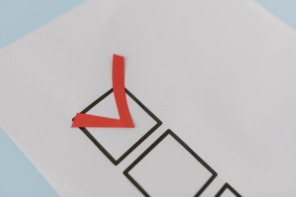Close-up of a checklist with a red checkmark made of paper on a white sheet, symbolizing task completion or approval, against a light blue background.