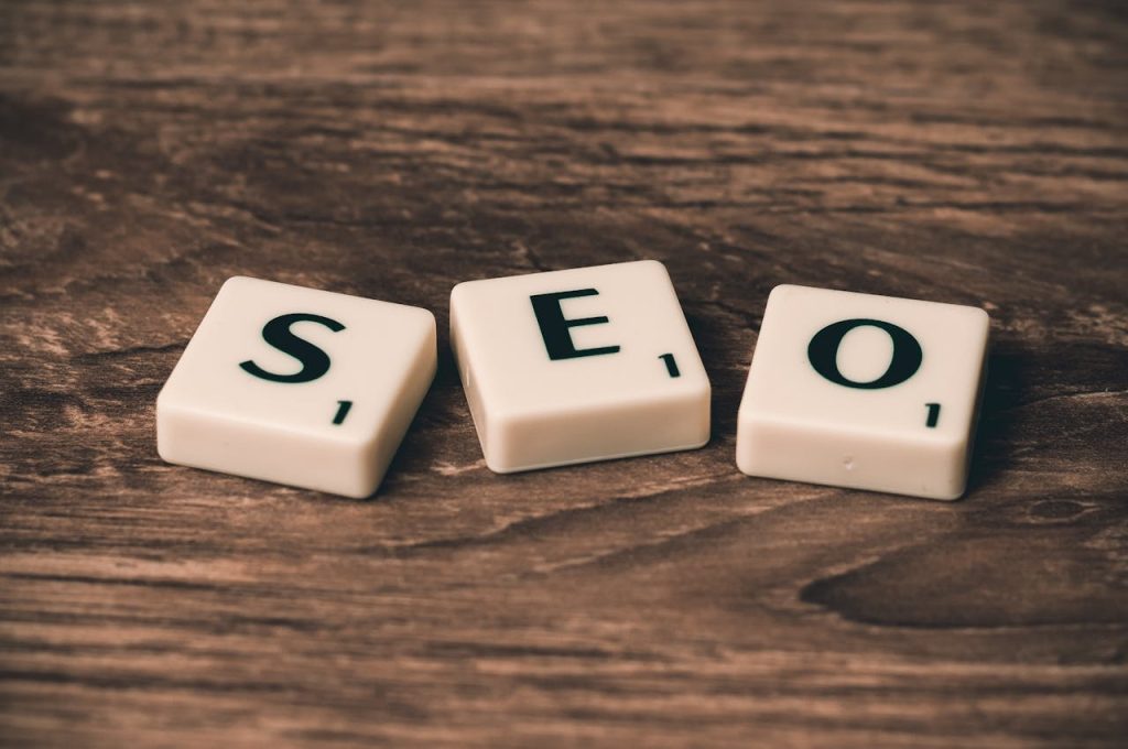 how to boost sales on etsy Three Scrabble tiles, with black letters on a white background, arranged on a rustic wooden surface that read SEO.
